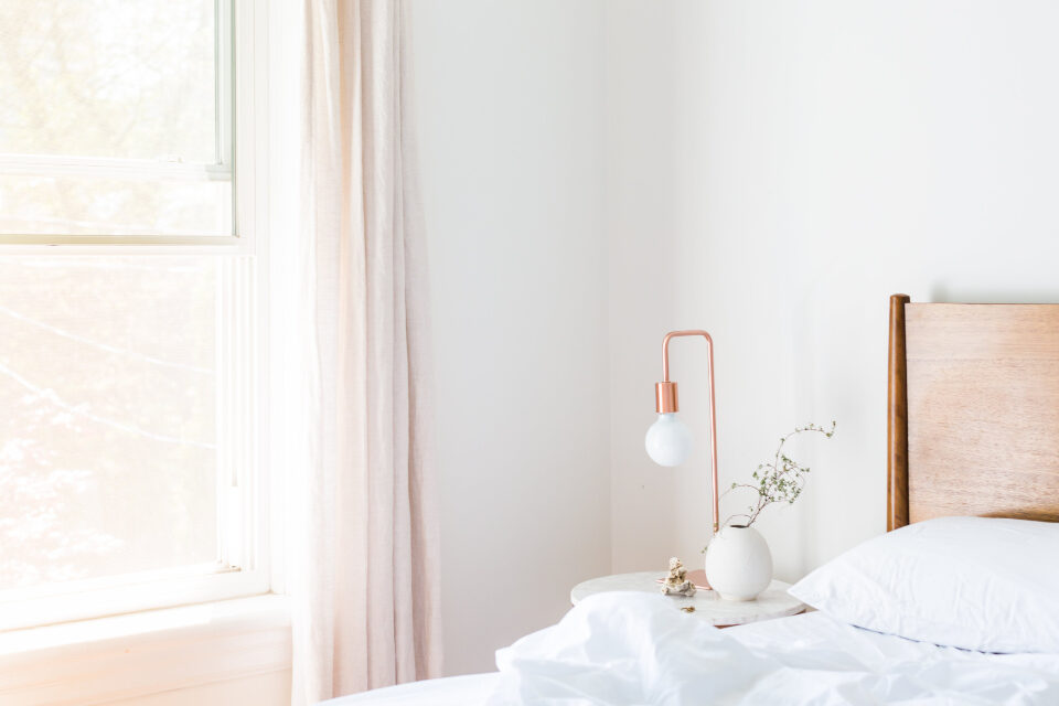 Bright bedroom with a white bed, a side table with flowers and a curtained window